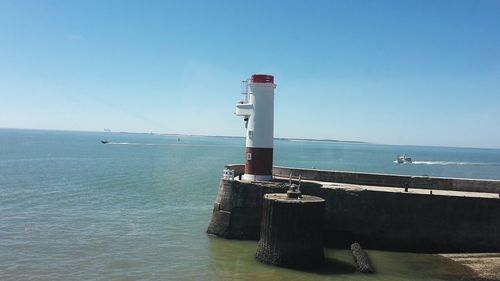 Lighthouse by sea against clear blue sky