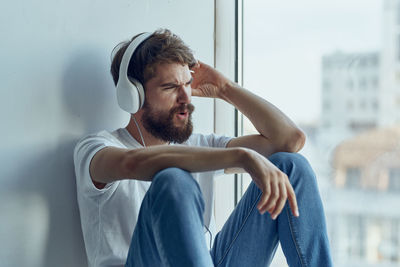 Man listening music while sitting by window at home