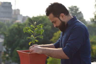 Side view of young man holding plant