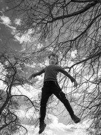 Low angle view of a kid, jumped up between bare trees