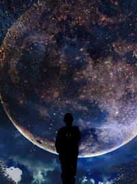 Rear view of silhouette man standing against sky at night