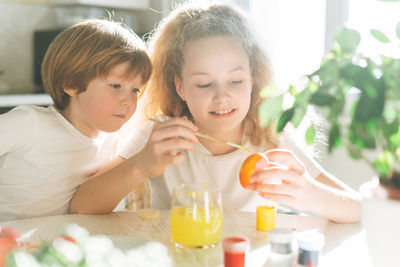 Two siblings brother and sister toddler boy tween girl painting easter eggs on kitchen at home 