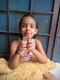 Close-up of girl eating chocolate against window