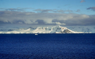 Scenic view of sea by snowcapped mountains against sky