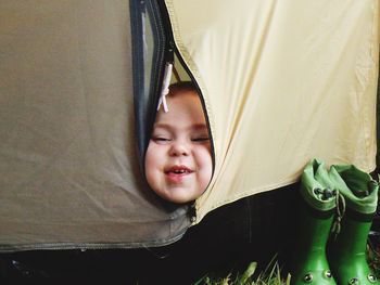 Portrait of smiling cute boy looking through tent zipper