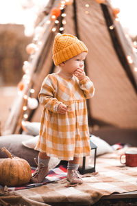 Stylish baby girl 2-3 year old wearing trendy dress and knit hat posing over light and decor outdoor