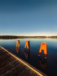 Rear view of woman sitting on pier over lake against clear sky during sunset