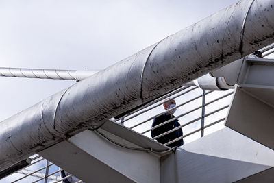 Low angle view of man standing by railing against sky