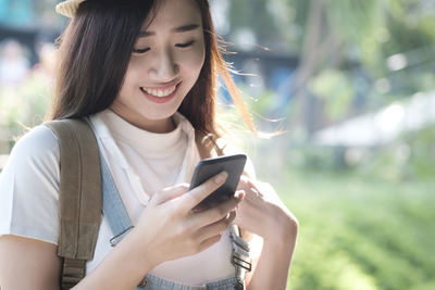 Smiling young woman using mobile phone while standing outdoors