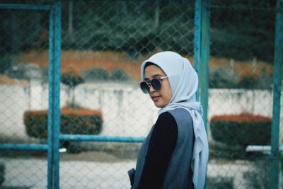 Side view of young man standing against fence