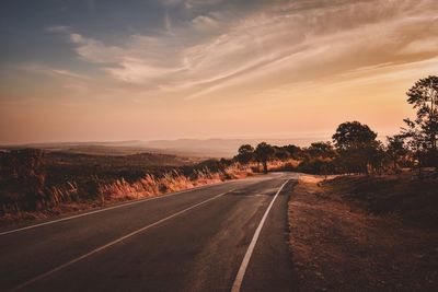 Road by trees against sky during sunset