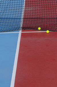 Two balls next to the net of a red tennis court