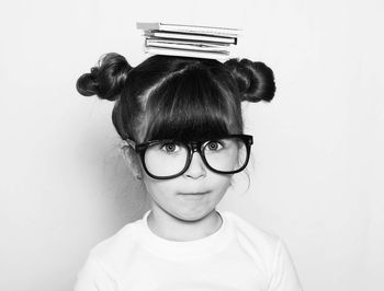 Portrait of cute nerd girl balancing books on head against white background