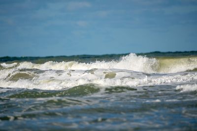 Waves rushing towards shore against sky