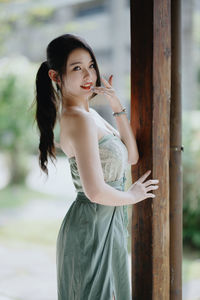 Portrait of young woman standing against tree trunk