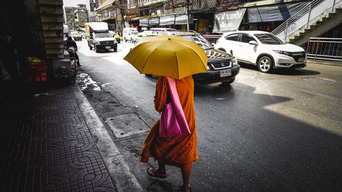 Rear view of monk walking under umbrella on street during sunny day