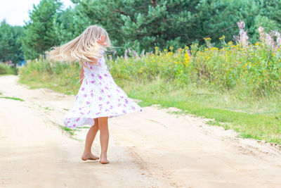 A girl with long blond curly hair is dancing, spinning on a forest road. childhood, happiness. 