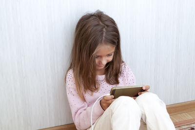 Young woman using mobile phone while sitting on wall