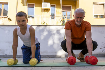 Low angle view of senior man with grandchild lifting dumbbells outdoors