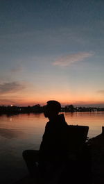 Silhouette man sitting on beach against sky during sunset