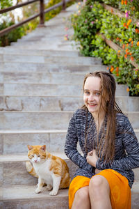 Girl sitting with cat sitting on staircase outdoors