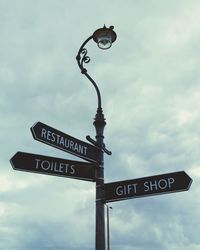 Low angle view of directional sign against cloudy sky