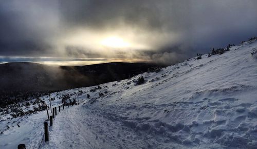 Scenic view of snowcapped mountains against cloudy sky during sunset