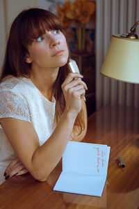 Thoughtful woman with book and pen sitting at table