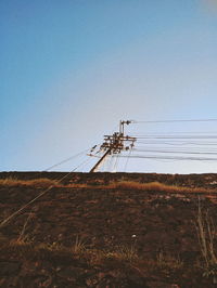 Low angle view of electricity pylon on field against clear sky