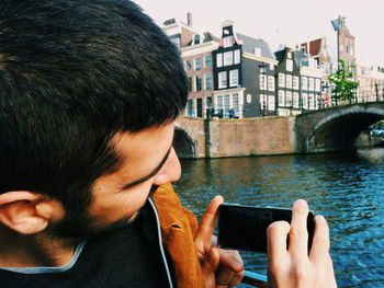 Close-up of man photographing bridge over river in city