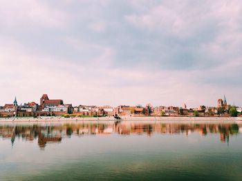 Residential district reflected in lake against cloudy sky