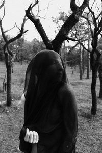 Woman covered in scarf while standing on field against bare trees