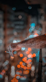 Close-up of hand holding cigarette against illuminated city