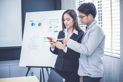 Colleagues using mobile phone while standing in office