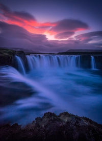 Scenic view of waterfall against dramatic sky during sunset