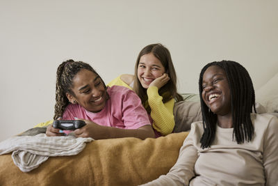 Cheerful teenage girl holding game controller while enjoying with female friends at home