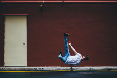 Full length of male dancer breakdancing on street by maroon wall