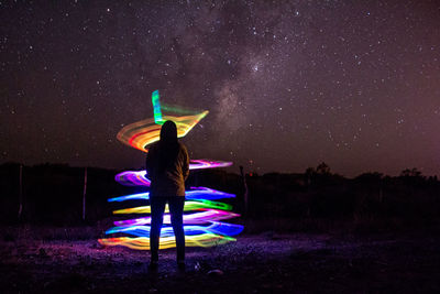 Rear view of woman looking at colorful light painting against star field at night