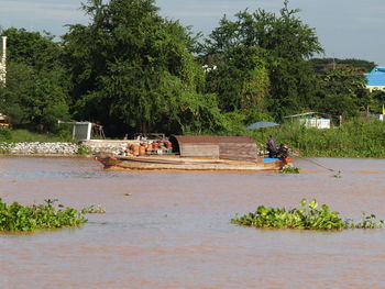People in boat by river against trees