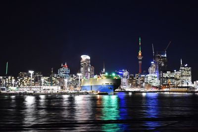 Illuminated cruise ship against modern buildings in city against sky at night