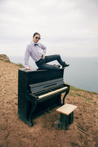 Woman in sunglasses and a white shirt sits on a black piano that stands on cape fiolent 