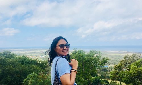 Smiling young woman standing by sea against sky