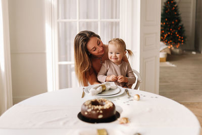 Happy mom and child are sitting at the dining table eating a christmas cupcake on holiday at home