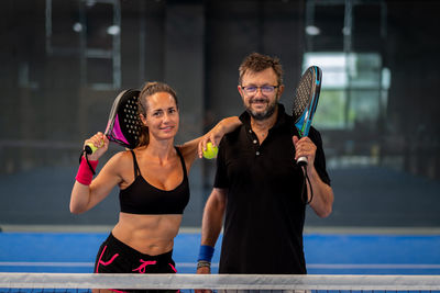 Portrait of two smiling sportsman's posing indoor on padel court with rackets and balls