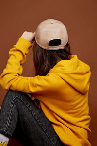 Rear view of woman wearing hat sitting against wall