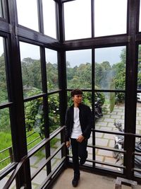 Full length portrait of young man standing against window