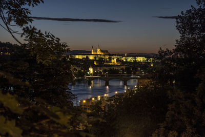 Illuminated bridge over river in city against sky at dusk