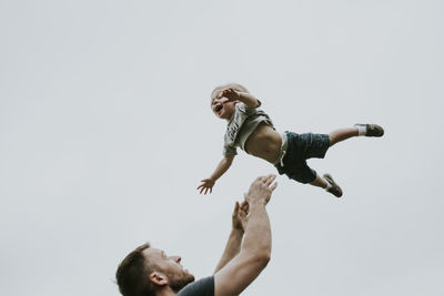 Playful father throwing son in air against clear sky