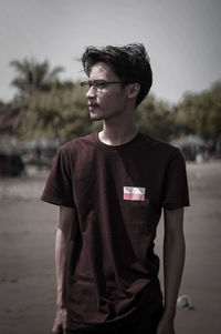 Young man looking away while standing outdoors