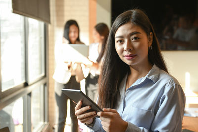 Portrait of woman holding smart phone while standing on laptop